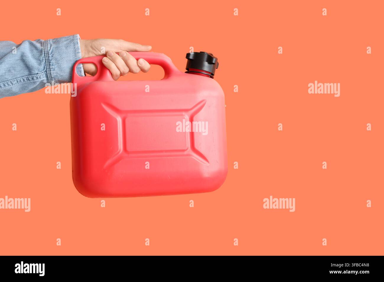 Krisensituation bei Kraftstoffen und hohe Benzinpreise, Hand, die einen roten Plastikkanister für Benzin auf orangefarbenem Hintergrund hält Stockfoto