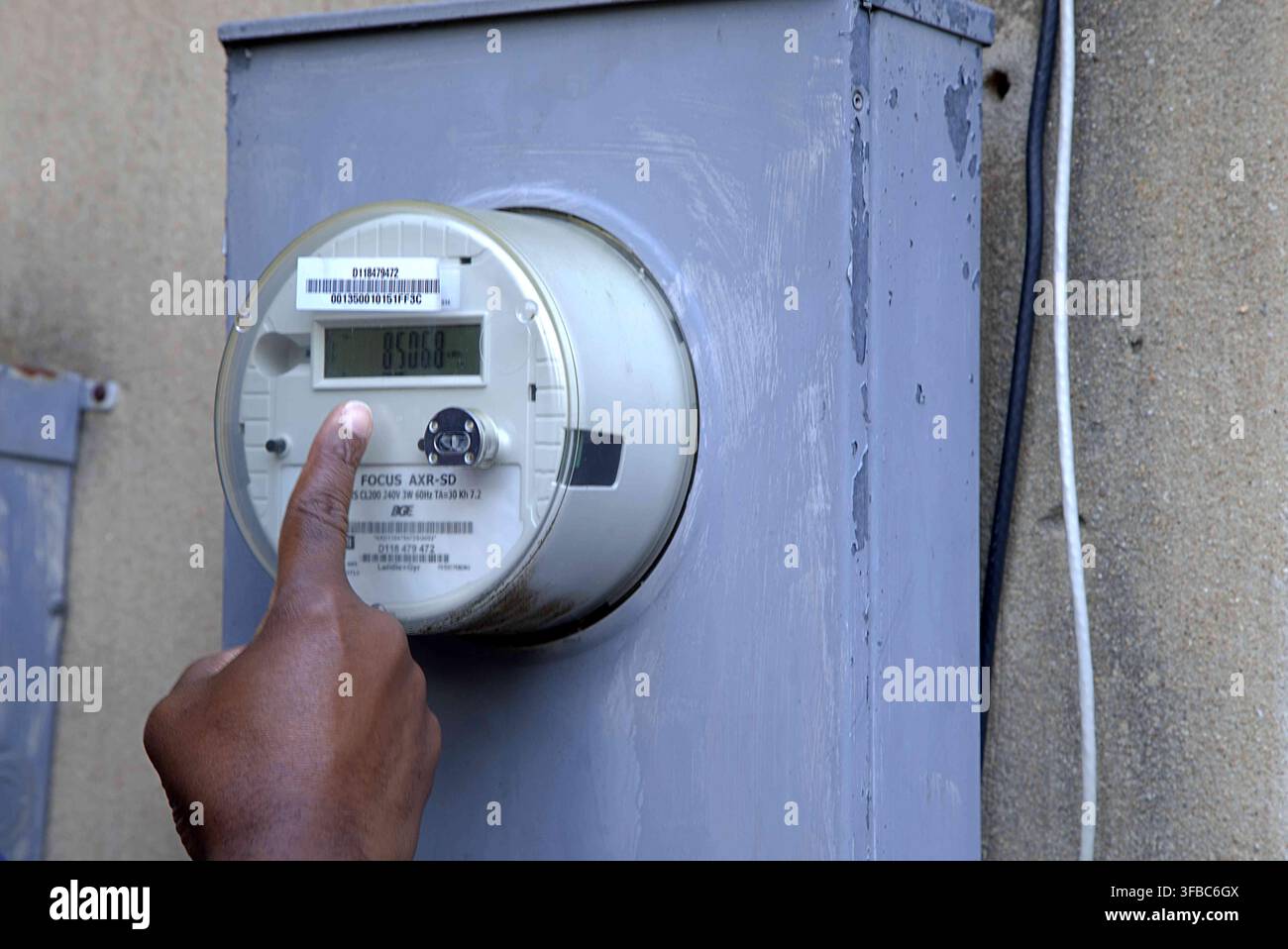 Eine Nahaufnahme einer Person, die Stromwerte überprüft oder einen digitalen intelligenten Stromzähler an einer Außenwand zurücksetzt. Stockfoto