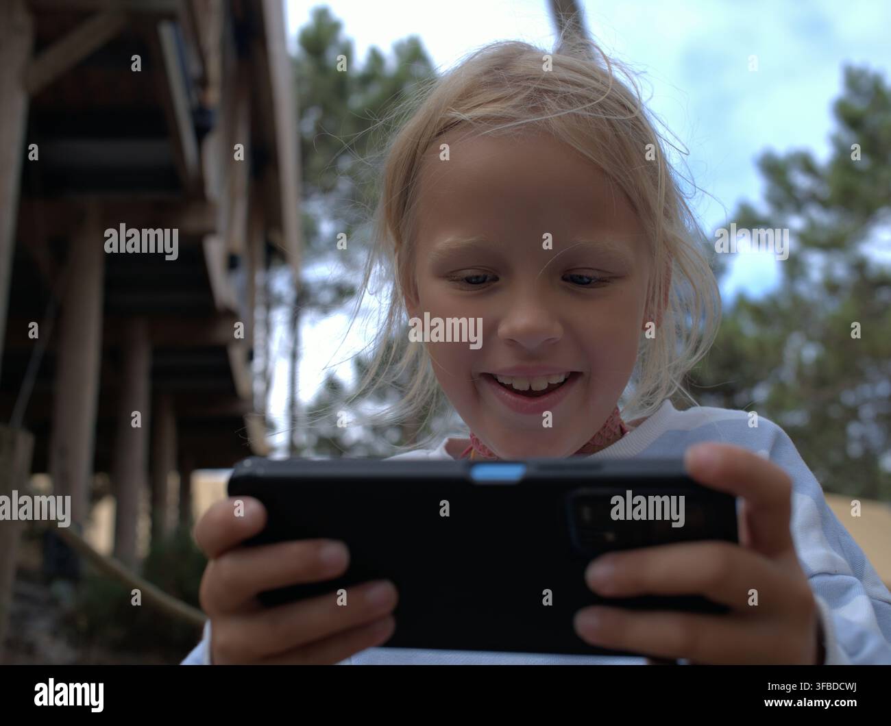 Mädchen lächelt strahlend, während es auf einer Handheld-Konsole spielt Stockfoto