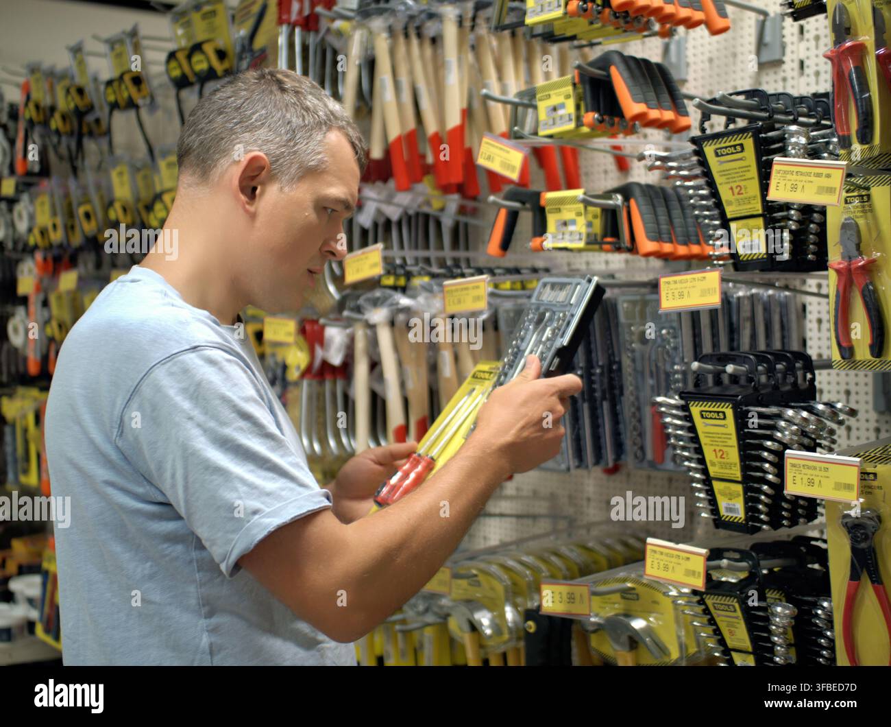 Mann, der ein Werkzeug von einer Wand in einem Baumarkt auswählt Stockfoto