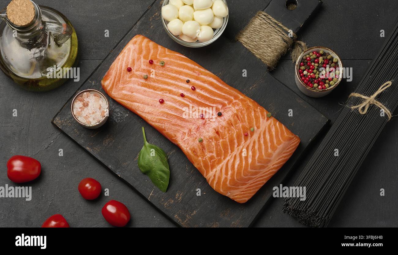 Zusammensetzung aus frischen Zutaten Lachsstück, Kirschtomaten, Mozzarella-Kugeln und schwarzen Nudeln. Schwarzer Tisch, Draufsicht Stockfoto