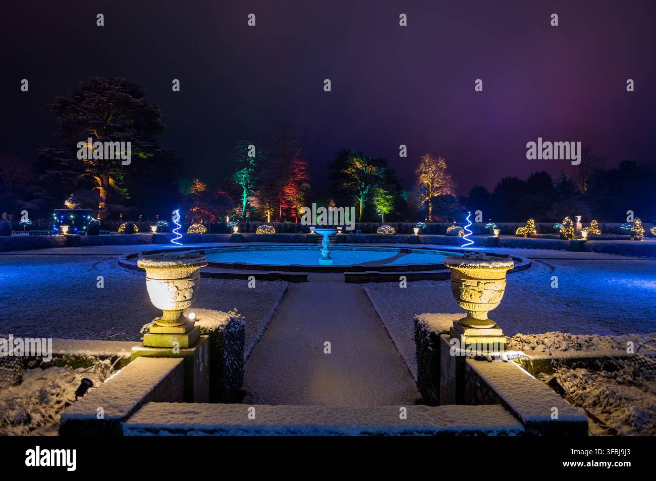 Schneebedeckter formeller Garten bei Nacht mit beleuchteten Bäumen und dekorativen Lichtern im Winter Stockfoto