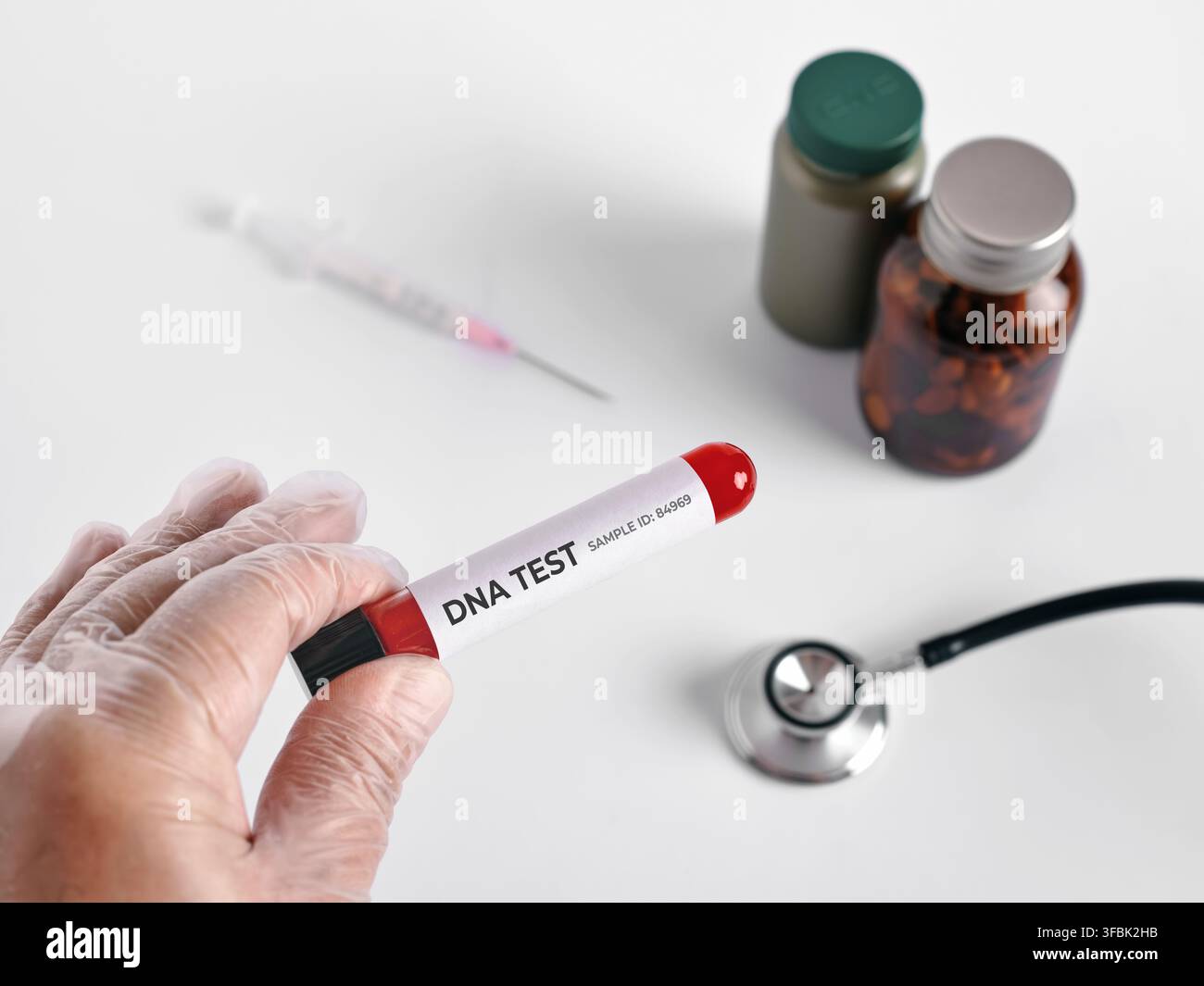 Geschützte Hand hält ein mit DNA-Test beschriftetes Blutprobenröhrchen mit medizinischen Geräten und Pillenflaschen auf weißem Hintergrund Stockfoto