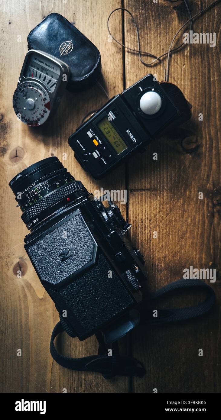 Bronica ETRS Mittelformat-Filmkamera mit austauschbarem Objektiv, Lichtmesser, Lederhülle und Kameragurt, die auf einem rustikalen Holztisch angeordnet sind, Illustration - Smartphone-aufgenommenes Stockfoto