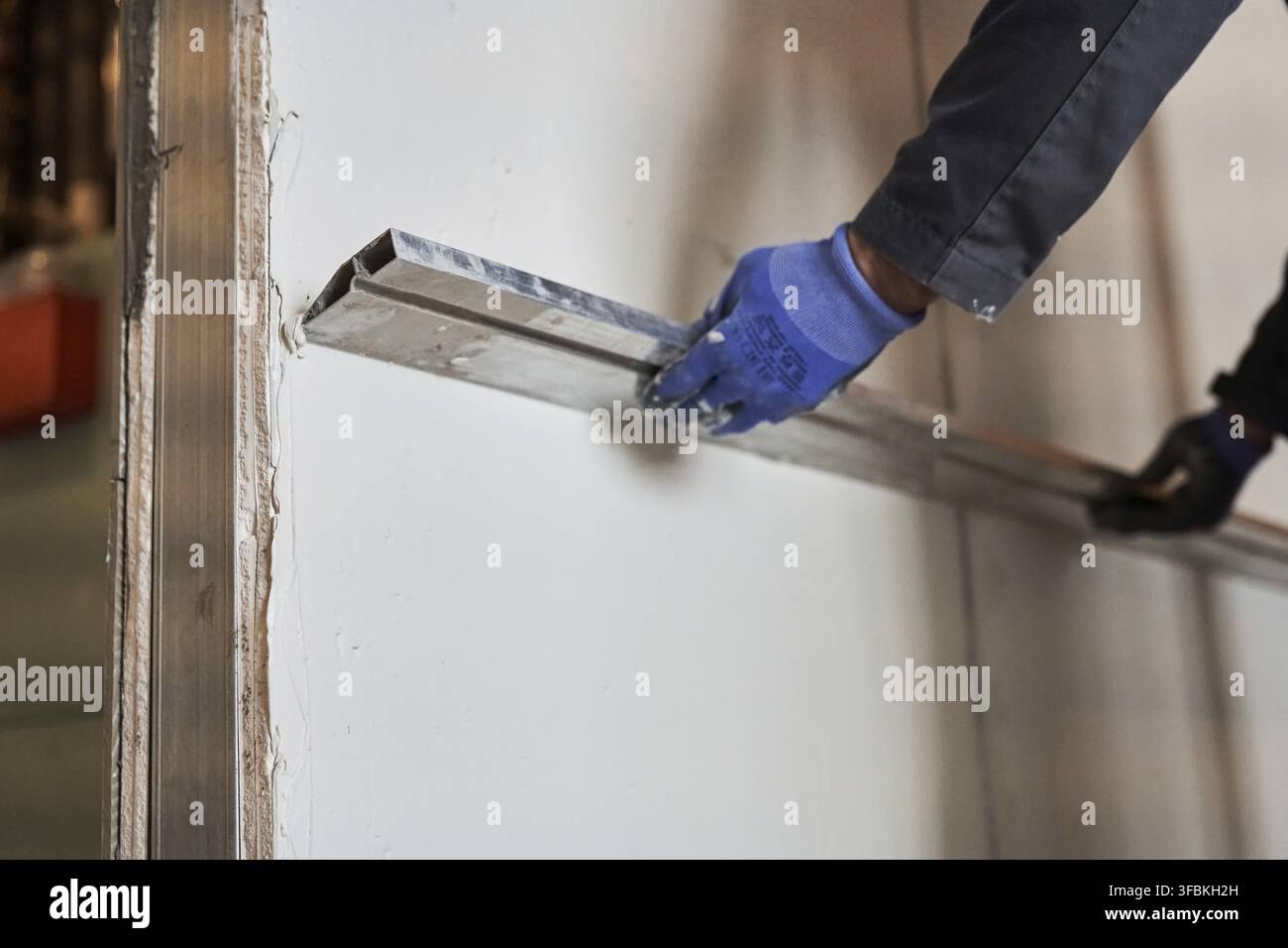 Das Regelwerkzeug für die Wandausrichtung. Ein Mann glättet eine Schicht Putz an einer Wand. Mit Platz zum Kopieren. Stockfoto