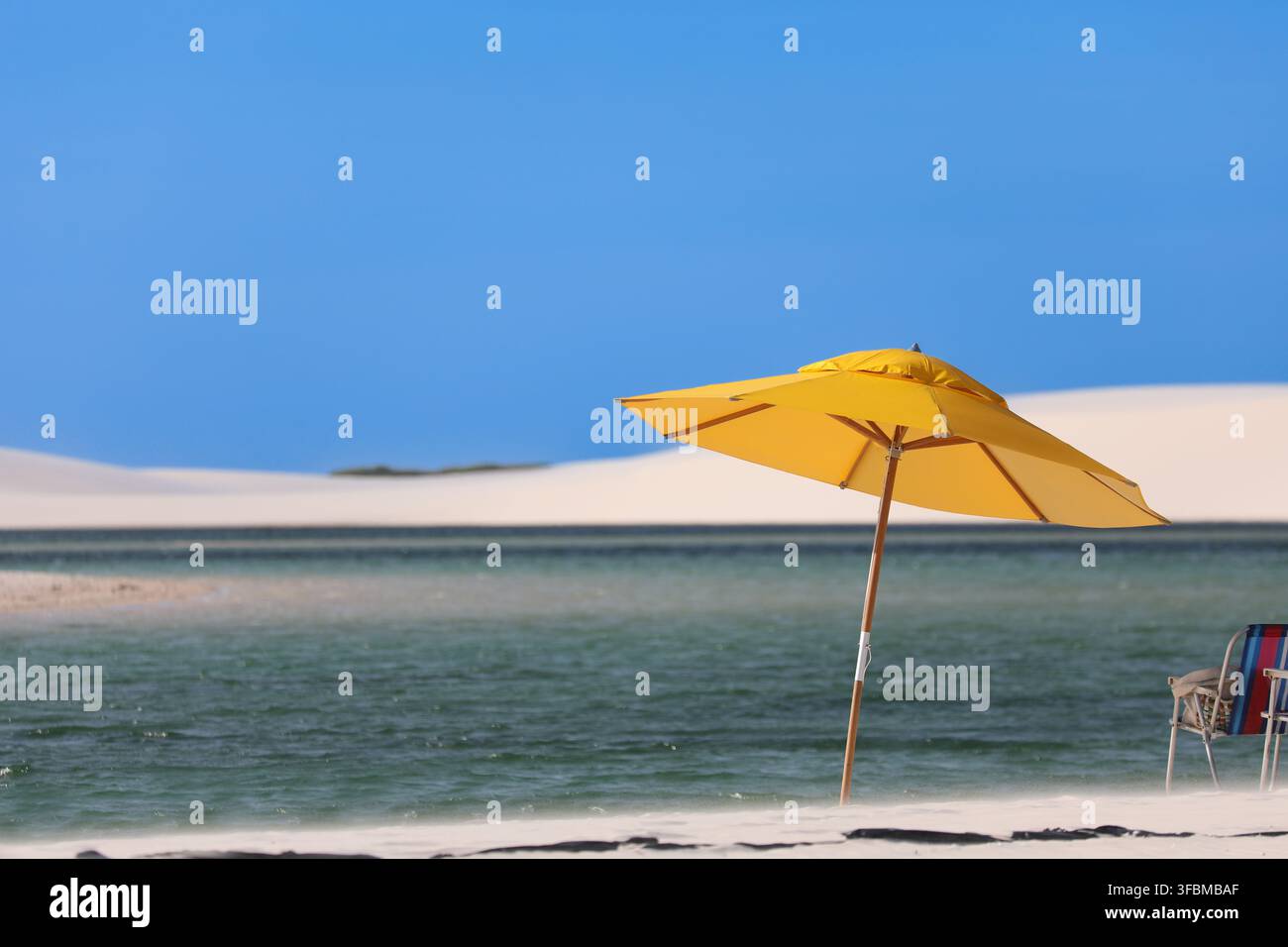 Gelbe Strandschirme und Strandliege an einem idyllischen Strand mit türkisblauem Wasser und Sanddünen. Stockfoto