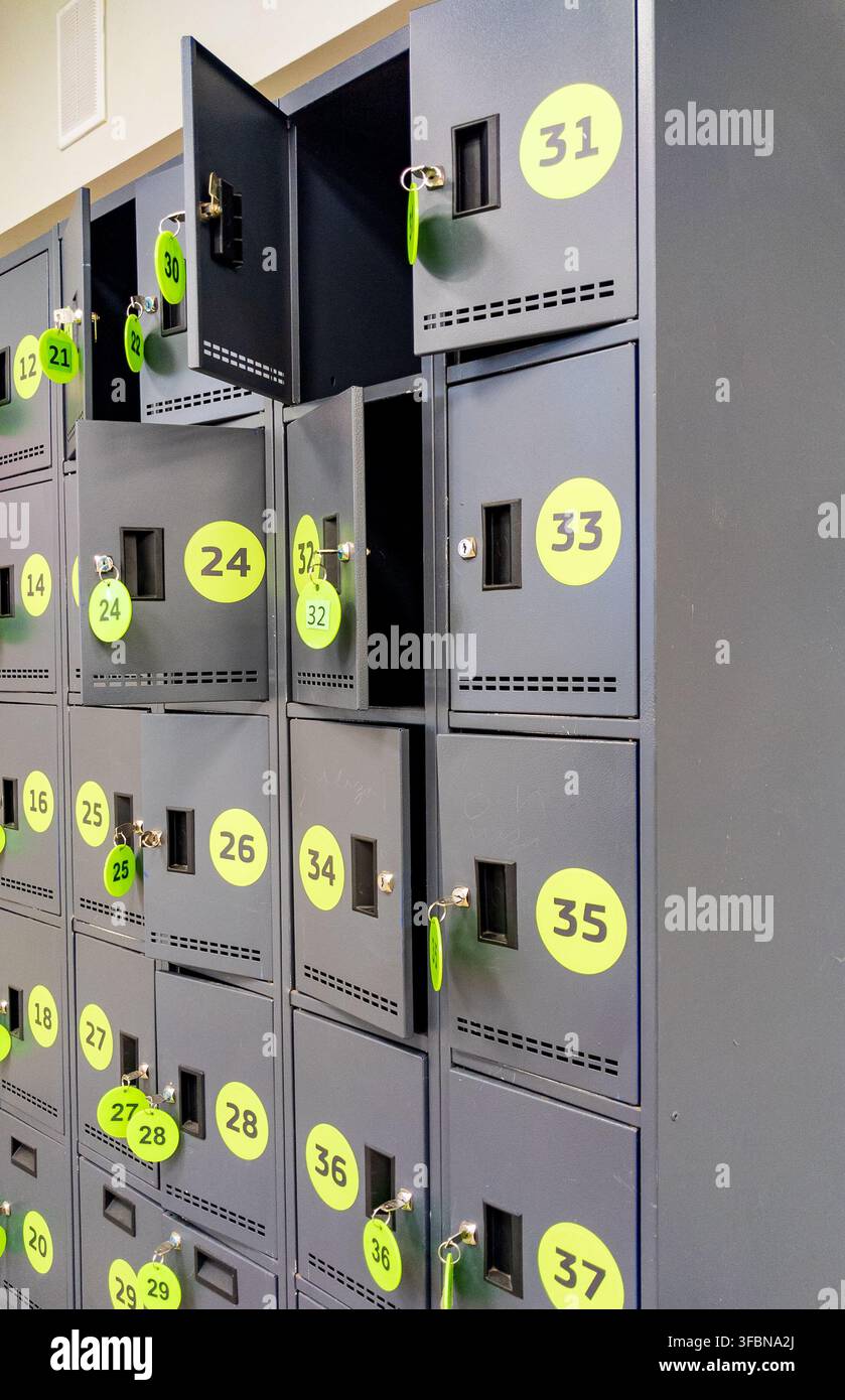 Dunkelgraues Metallschranksystem mit gelben runden Etiketten und eingelegten Schlüsseltaganhängern an offenen Türen. Konzept für sichere Lagerlösungen, Fitnessstudio-Umkleideräume, a Stockfoto