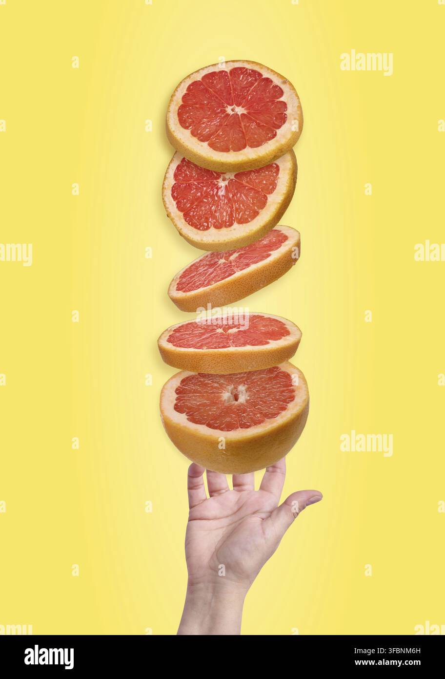 Fünf saftige rote Grapefruitscheiben schweben in der Luft über einer offenen Handfläche vor einem hellen gelben Farbverlaufshintergrund Stockfoto