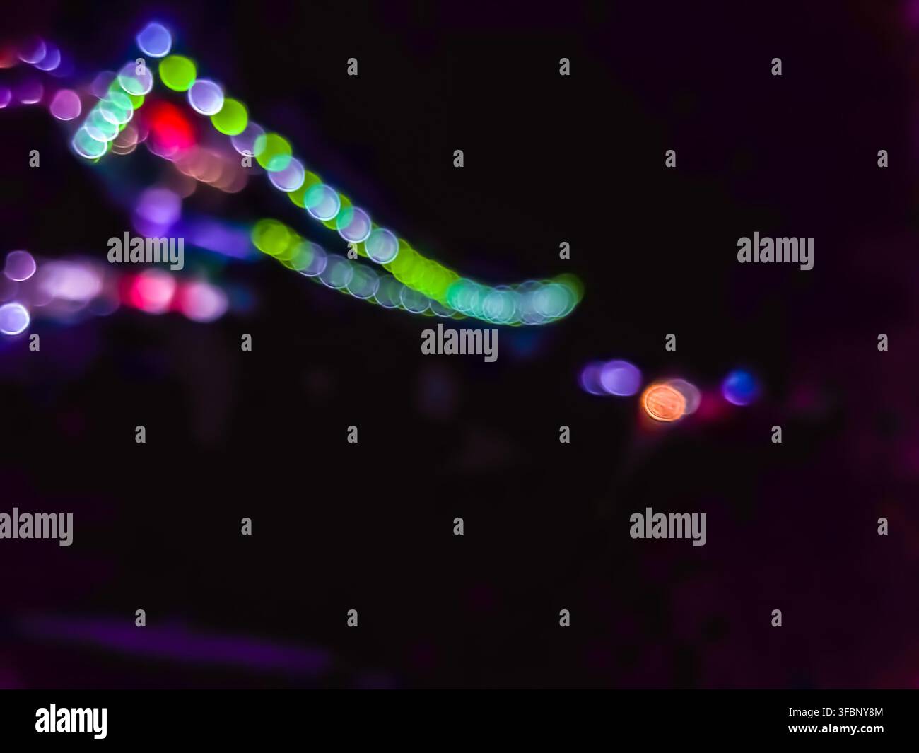 Abstrakter Bokeh-Hintergrund aus farbenfrohen Lichtern in der Nacht. Unscharf leuchtende runde Formen in Lila, Grün und Rosa, isoliert auf einem dunklen Hintergrund. Stockfoto