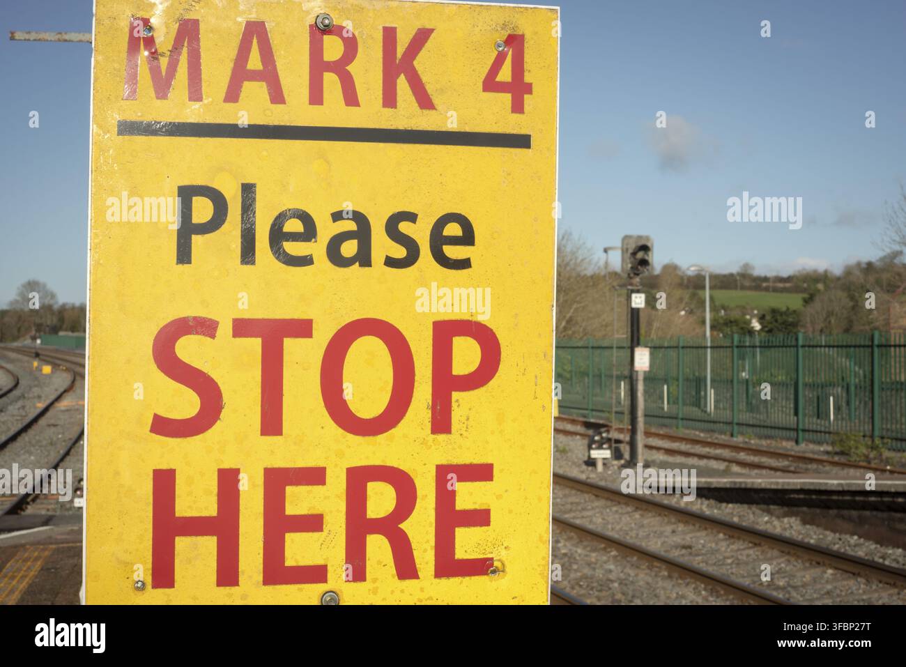 Bitte halten Sie hier am gelben Schild am Bahnhof oder Bahnsteig in Irland als Warnung, die Gleise nicht zu überqueren Stockfoto