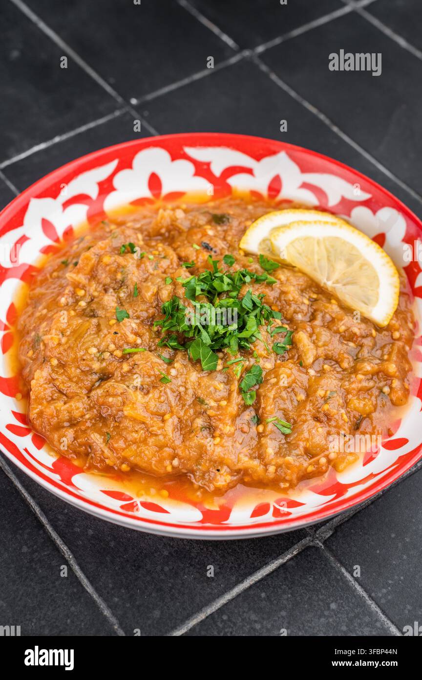 Klassischer indischer Auberginen-Bharta vegetarischer Auberginen-Curry-Dip serviert in dekorativer roter Platte mit Zitronengarnitur dunklem Hintergrund Lebensmittelfoto Stockfoto