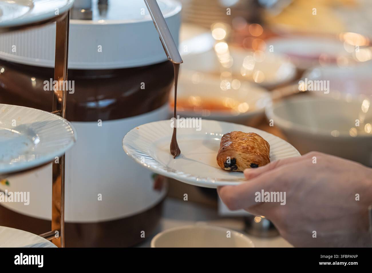 Mann verwendet einen Spender, um Schokoladenspread aus einem großen Glas auf einen Teller zu drücken, und zeigt die praktische Zubereitung von Lebensmitteln. Stockfoto