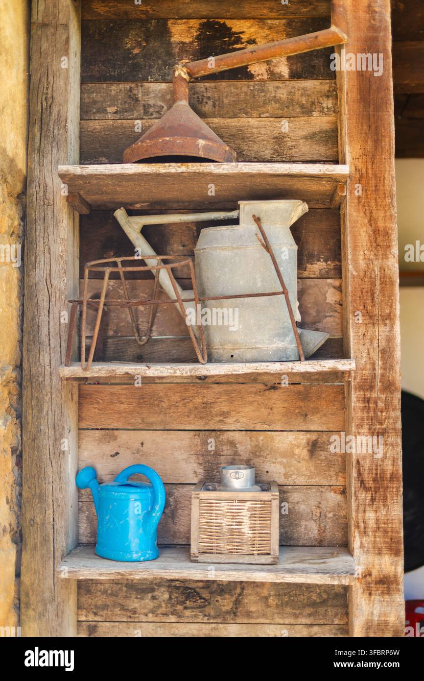 Vintage-Gießkannen und rostiger Trichter auf rustikalem Holzregal Stockfoto