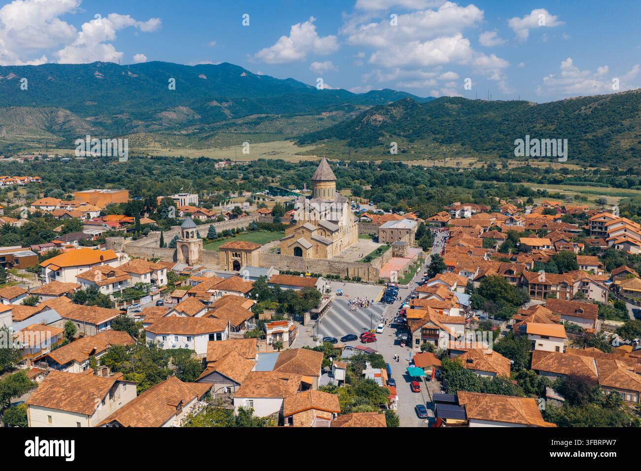 Luftaufnahme der historischen Svetitskhoveli-Kathedrale, umgeben von Terracotta-Dächern und üppigen Bergen in Mtskheta, Mtskheta-Mtianeti, Georgien. Stockfoto