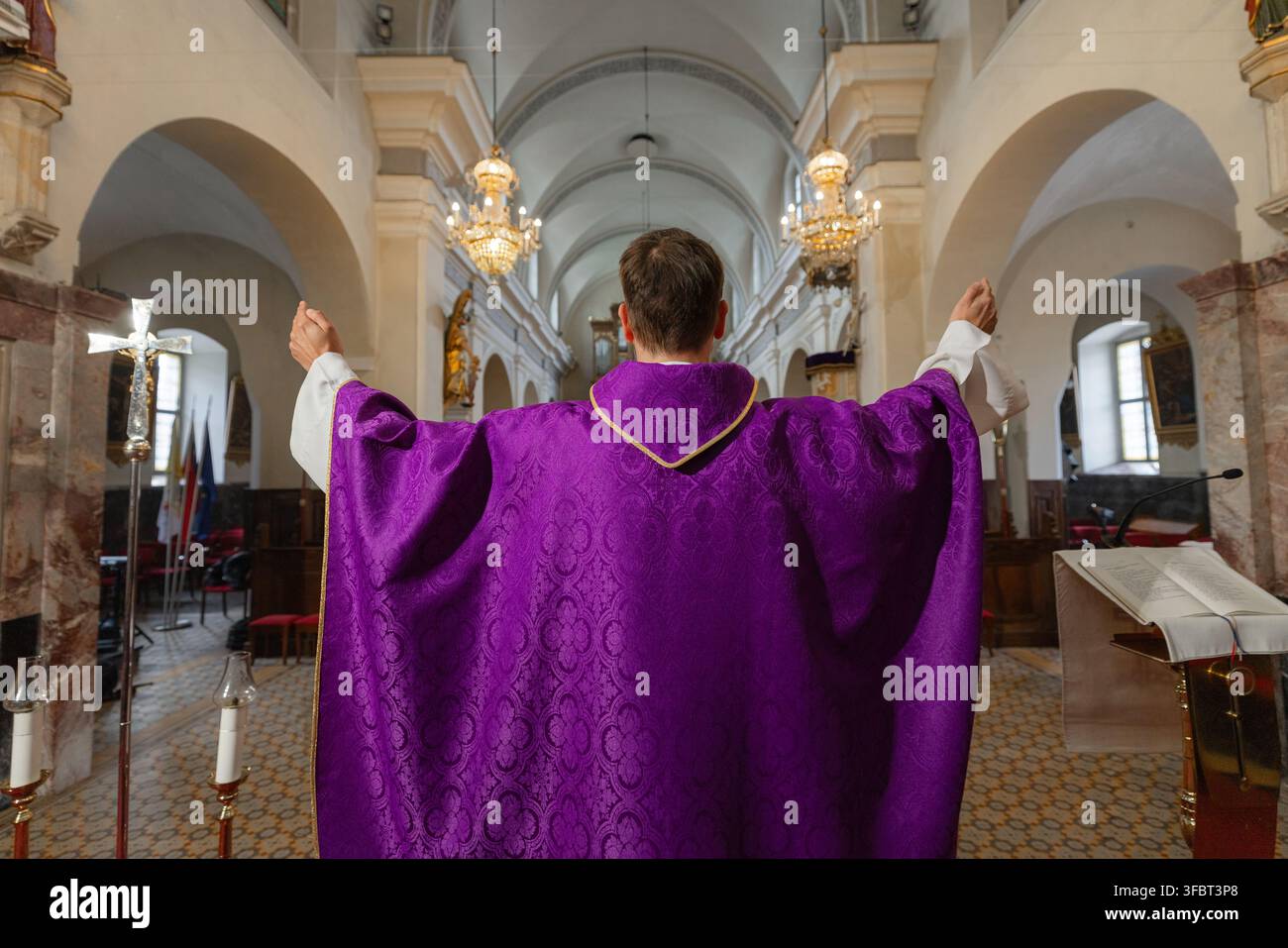 Ein Priester steht mit erhobenen Armen in einer katholischen Kirche während der heiligen Messe. Der Gottesdienst findet an einem europäischen Ort statt. Stockfoto