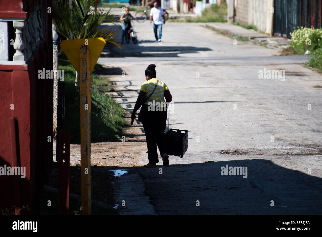 Rückansicht einer Frau, die eine rollende Kiste die Straße hinunter in Ciego de Avila, Kuba, im August 2026 zieht Stockfoto