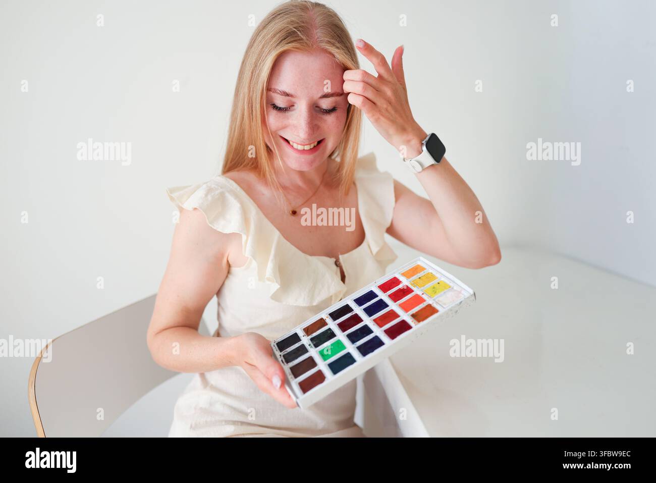 Lächelnde junge Frau hält eine bunte Aquarellpalette und genießt das Malen als kreatives Hobby zu Hause. Stockfoto