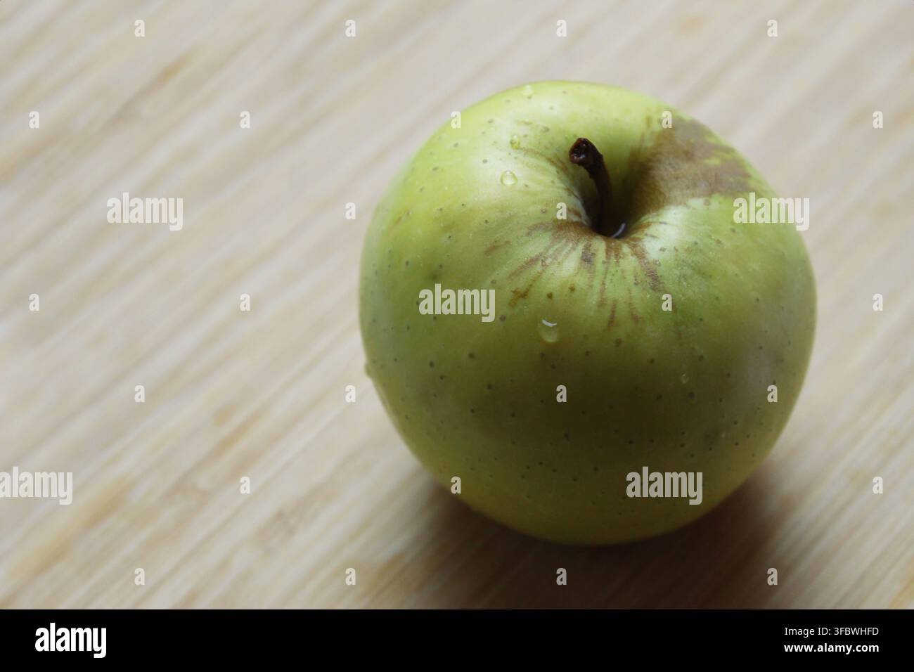 Nahaufnahme eines Granny-Smith-Apfels (Malus domestica) mit Wassertropfen vor einem Holz-Hintergrund. Konzept: lecker, Obst, frisch, Mittagessen, Hausapfel Stockfoto