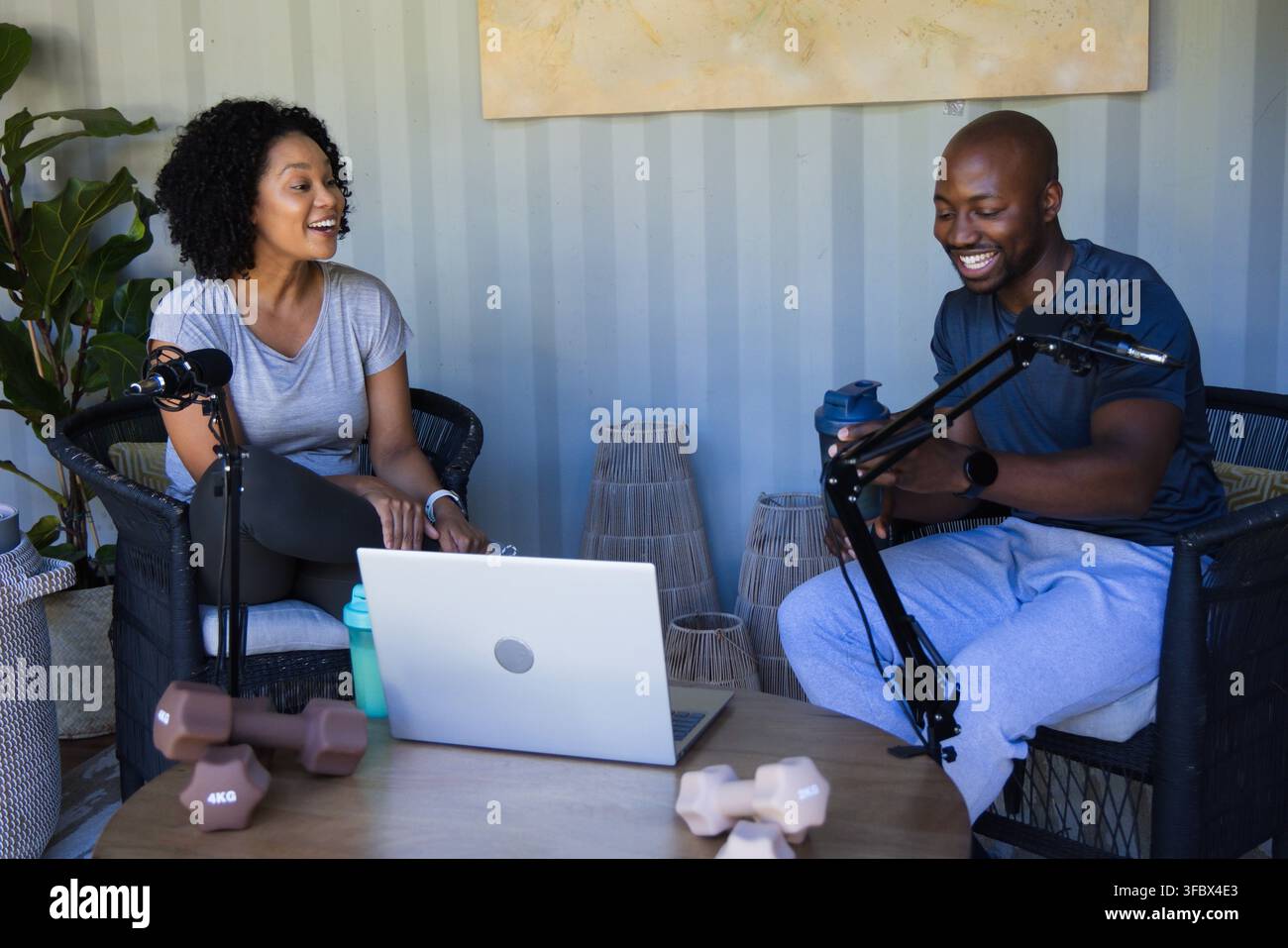 Afroamerikanische Co-Moderatoren, die sich in der Home-Recording-Ecke gegenüberstehen und Laptop und Mikrofone verwenden Stockfoto