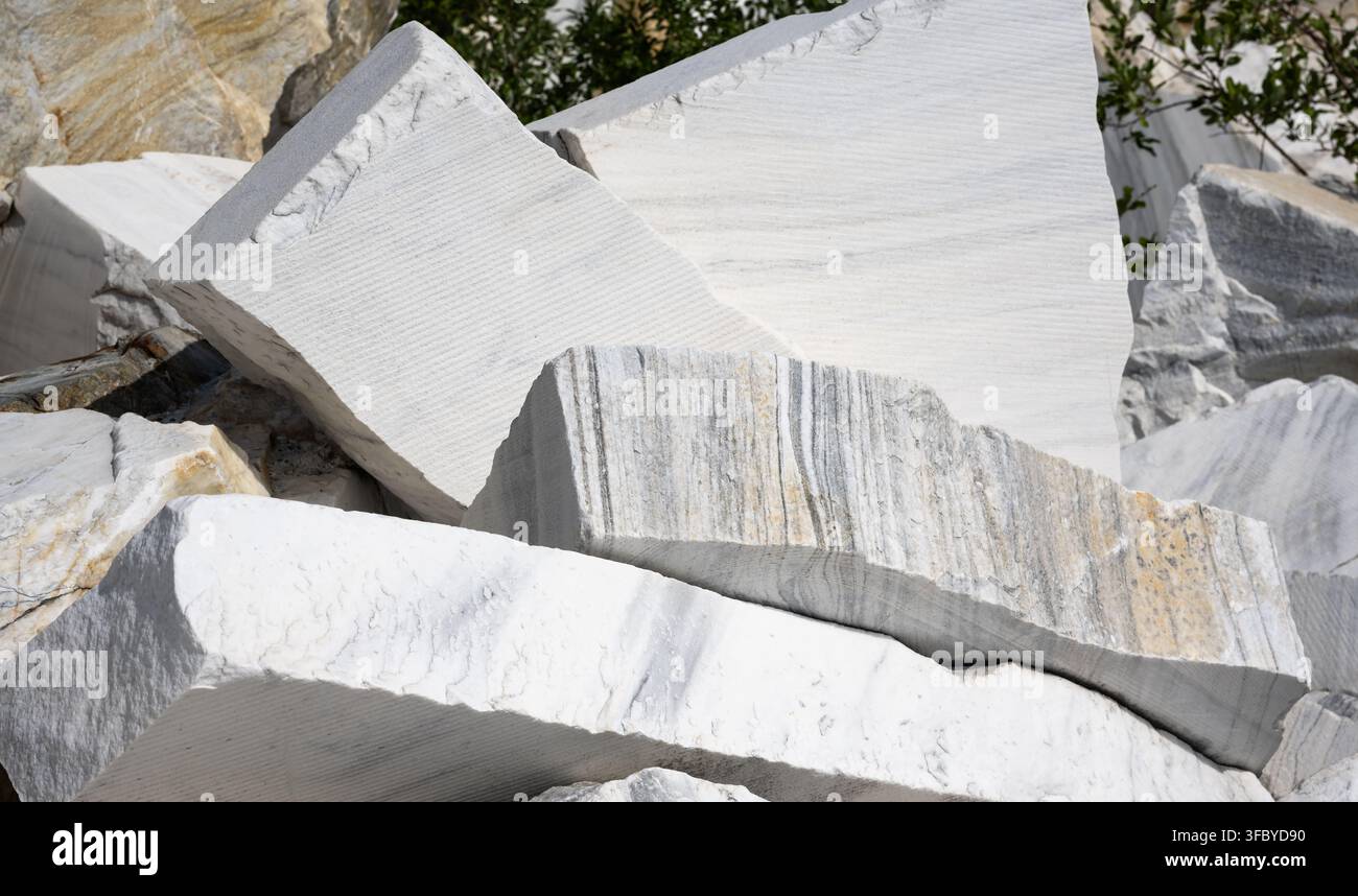 Große rohe weiße Marmorblöcke, die in einem Steinbruch gestapelt sind. Ungeschliffene Natursteinplatten mit grauen Adern und rauen Texturen. Industrieller Bergbau und Bau Stockfoto