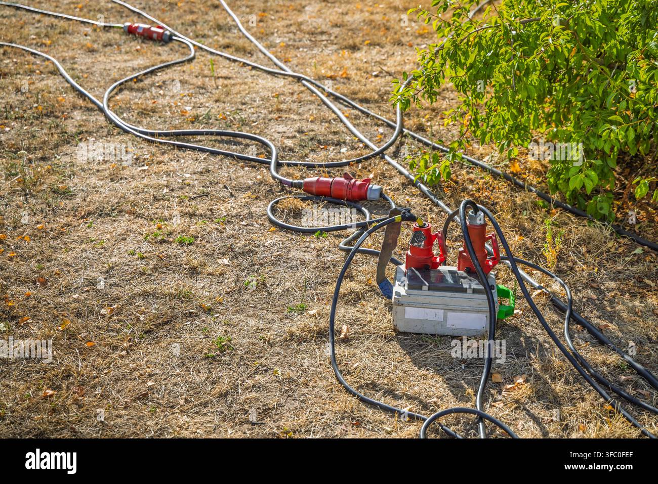 Schwere Industrie-Stromkabel und Verbinder, die auf dem Boden ausgelegt sind, was eine Stromversorgung im Freien für Geräte oder Veranstaltungen nahelegt Stockfoto