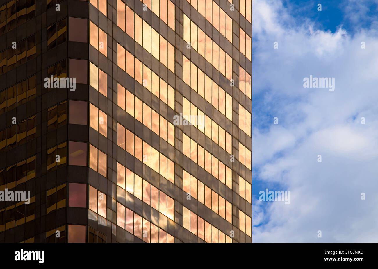 Ecke eines Hochhaus-Bürogebäudes mit bronzefarbenen Glasfenstern, die Wolken vor einem hellblauen bewölkten Himmel reflektieren. Stockfoto