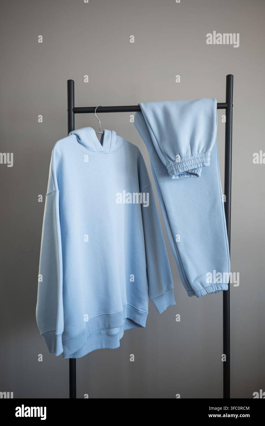 Ein weicher blauer Hoodie liegt neben passenden Jogginghosen auf einem schwarzen Regal in einem schlichten Innenraum. Stockfoto