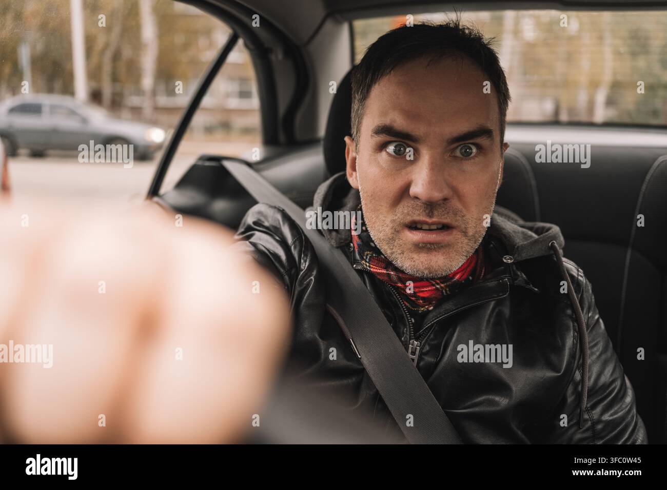 Wütender männlicher Fahrer, der aggressiv schreit und gestikuliert, während er hinter dem Steuer sitzt. Straßenwut, gestresstes Fahren und wütende Reaktion auf den Verkehr. Stockfoto