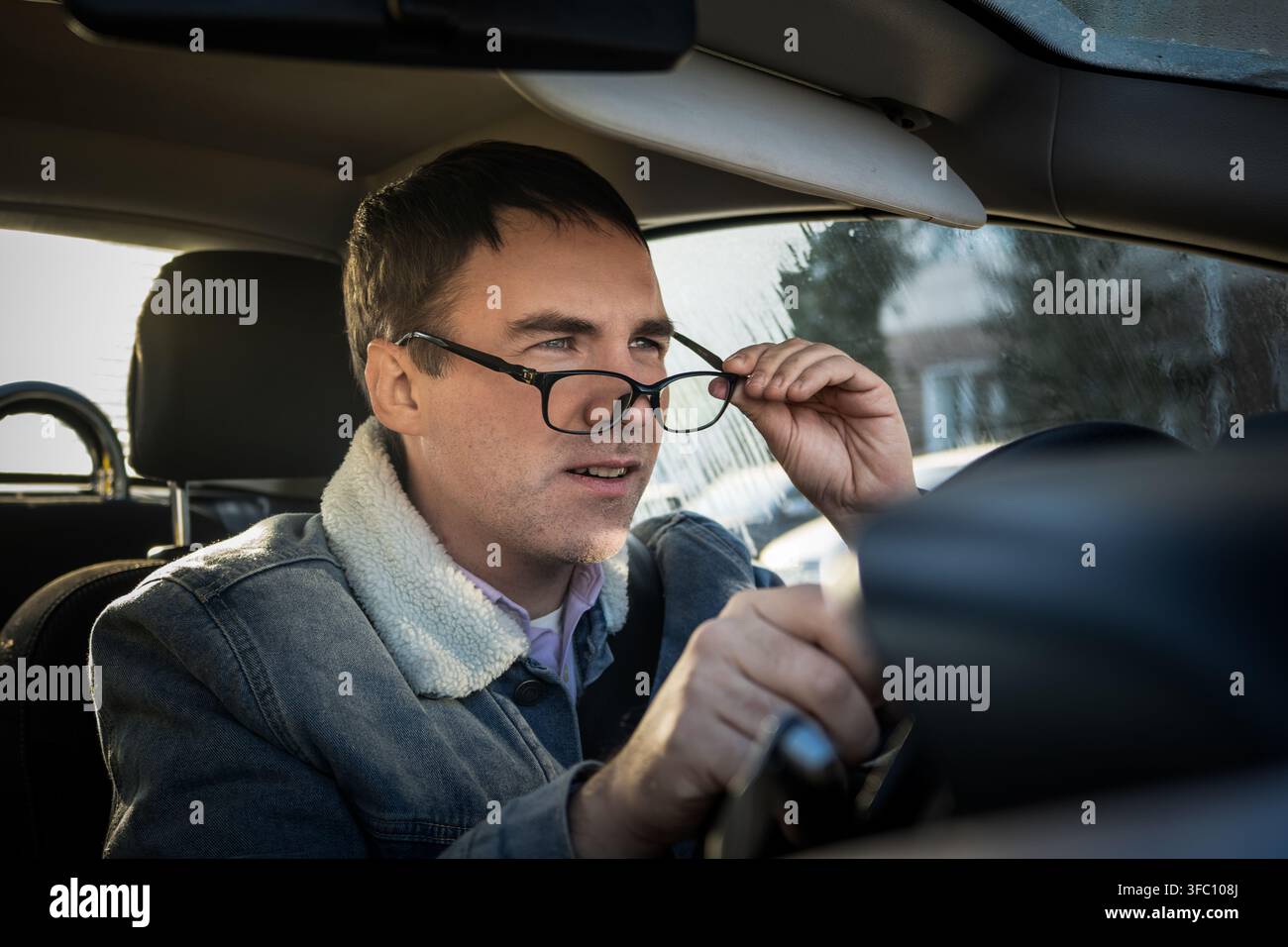 Männlicher Fahrer, der seine Brille anpasst und mit konzentriertem Ausdruck nach vorne schaut, während er fährt. Korrektur der Sicht, Aufmerksamkeit auf die Straße und Sicherheit Stockfoto