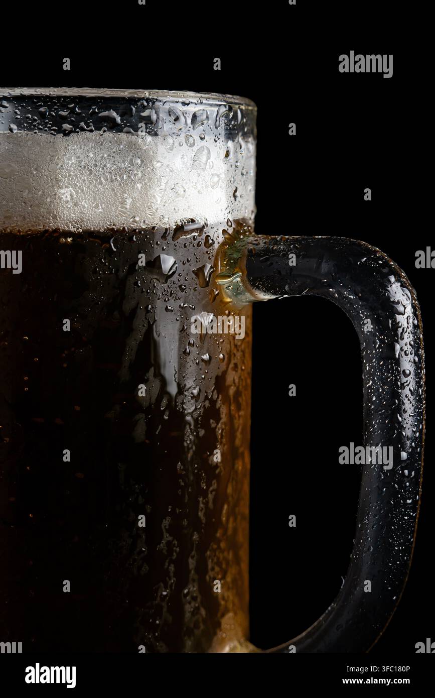 Ein Bierkrug ist gefüllt und kalt mit Schaum oben. Wassertropfen bedecken das Glas. Die Szenerie ist dunkel und fängt einen geselligen Moment ein. Stockfoto