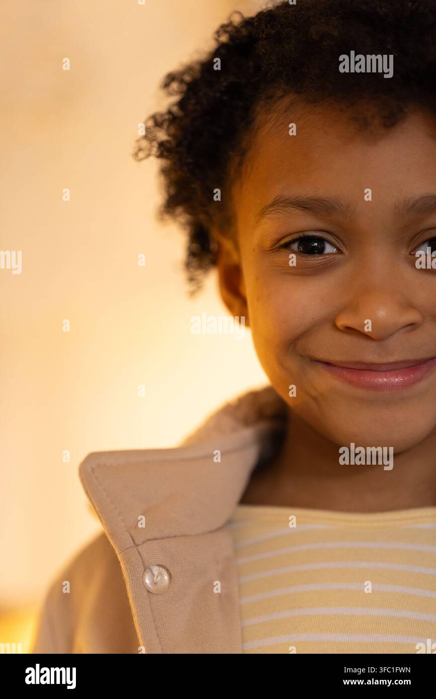Afroamerikanisches Kind lächelt, trägt einen beigen Mantel mit Knopf und ein gelb gestreiftes Hemd im Studio Stockfoto