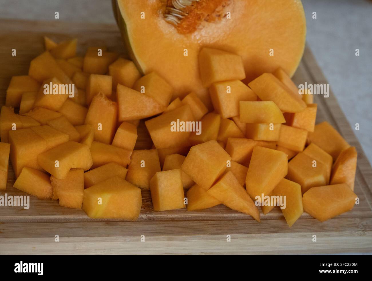 Frischer Butternusskürbis in Würfeln und Keilen auf einem Holzschneidebrett. Nahaufnahme einer Essenszubereitung mit orangefarbenem Winterkürbis, Samen und Scheibe Stockfoto