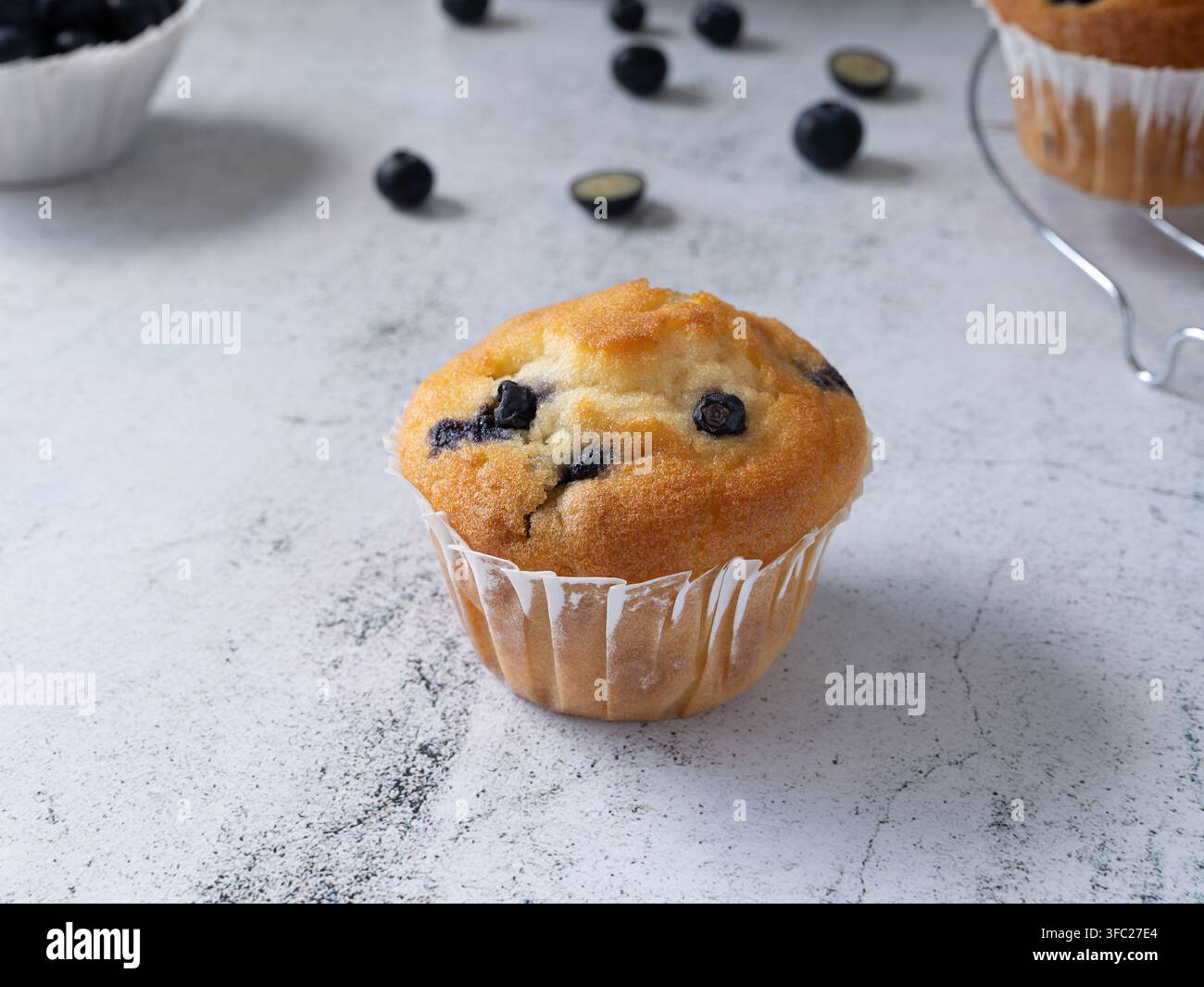Hausgemachter Blaubeermuffin, fotografiert auf einer hellen Steinfläche mit frischen Blaubeeren und Backzutaten Stockfoto