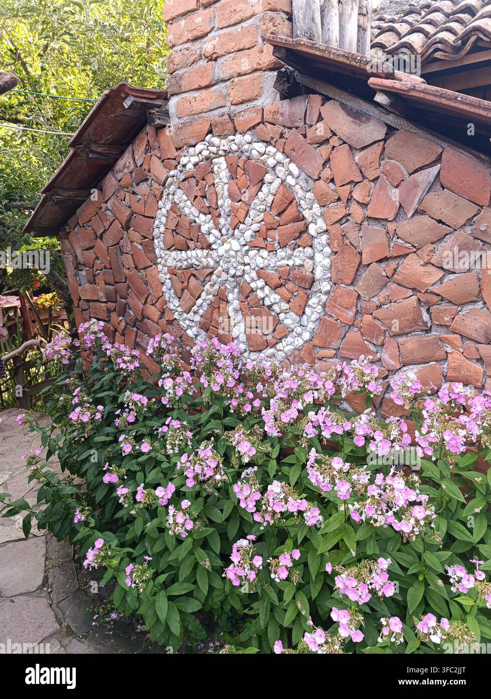 Rustikale Ziegelwand und rosa Blumen in einem bezaubernden Garten - Smartphone-aufgenommenes Stockfoto