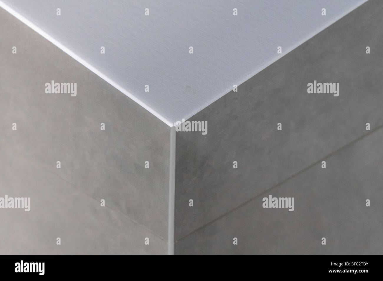 Eine minimalistische Komposition, die sich auf die Schnittstelle zweier texturierter grauer Oberflächen und einer glatten weißen Ebene konzentriert, um ein Gefühl von Tiefe und modernem Design zu erzeugen Stockfoto