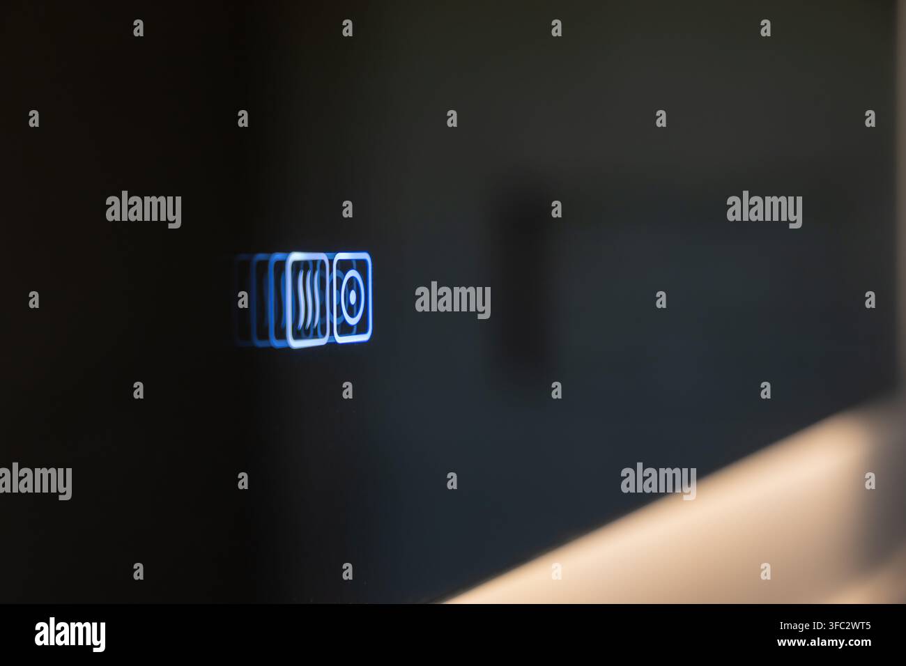Nahaufnahme einer glatten schwarzen Oberfläche, die beleuchtete blaue Symbole anzeigt, die Hitze- und Audiofunktionen darstellen, was fortschrittliche Technologie suggeriert Stockfoto
