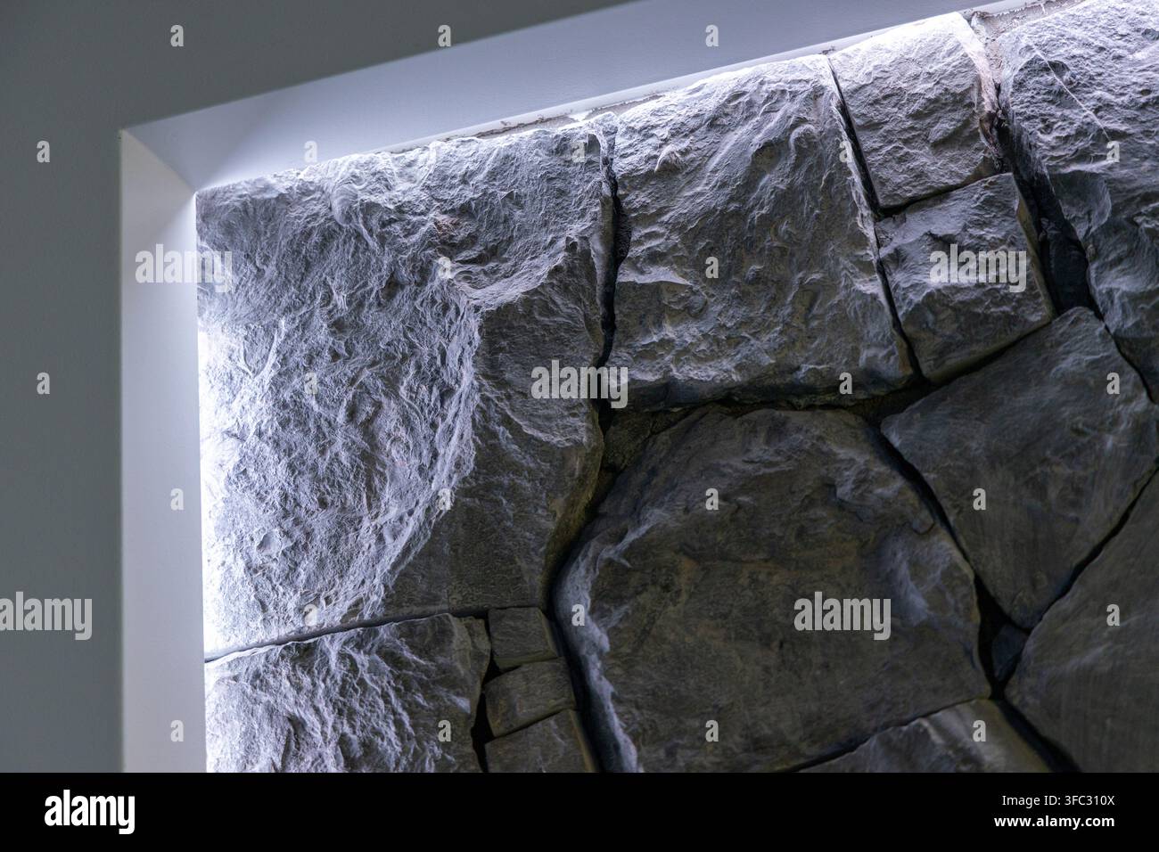 Nahaufnahme einer rauen, unebenen Steinmaueroberfläche, die von weichem seitlich einfallendem Licht beleuchtet wird, wodurch ihre raue Textur und tiefe Spalten betont werden Stockfoto