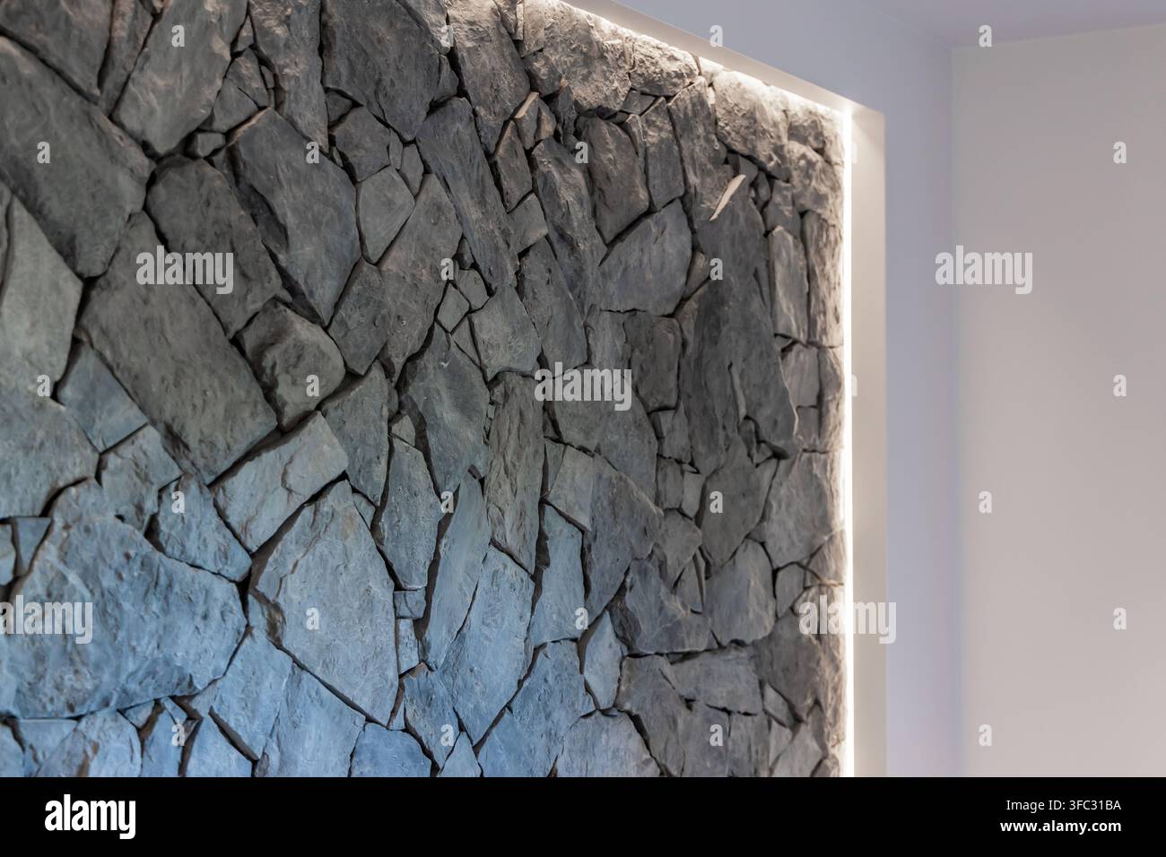 Eine Nahaufnahme eines natürlichen Steinwand-Innenarchitekturelements, das durch weiches, integriertes Licht entlang des Randes betont wird Stockfoto