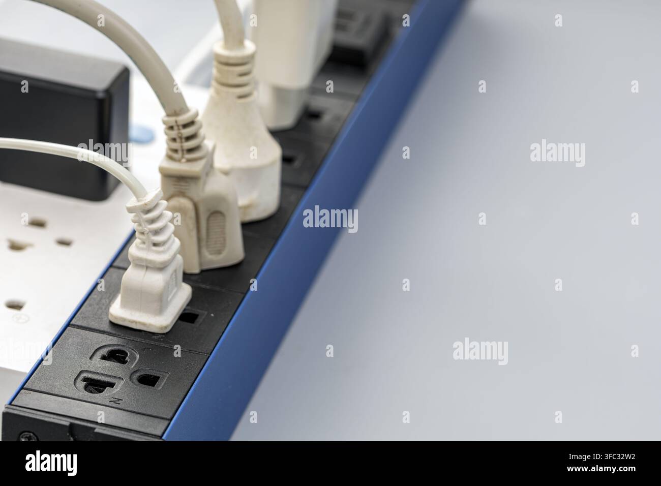 Mehrere weiße Stromkabel, die in eine schwarze und blaue Steckdosenleiste eingesteckt sind, zeigen Geräteanschlüsse und Steckdosenutzung. Stockfoto