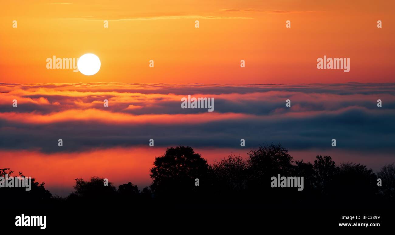 Ruhiger Sonnenaufgang und tiefer orangefarbener Himmel über welligem Nebel oder Wolken. Faszinierendes Wetterphänomen mit wunderschönen lebendigen Farben. Stockfoto