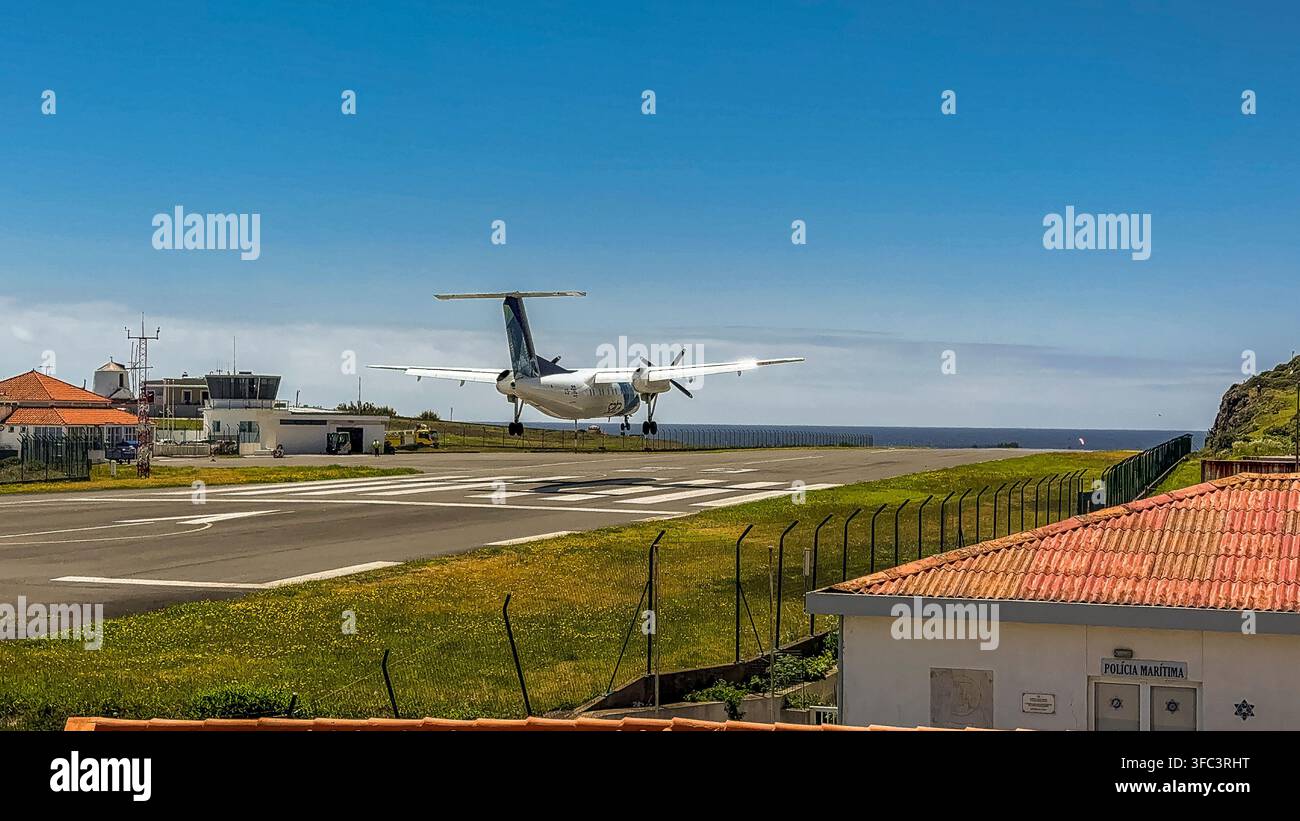 Corvo, Azoren, Portugal Kleines Propellerflugzeug landet auf einer Landebahn in der Nähe eines Küstendorfes. Rotgedeckte Dächer und grüne Felder rahmen die Szene ein. Klares Blau s Stockfoto