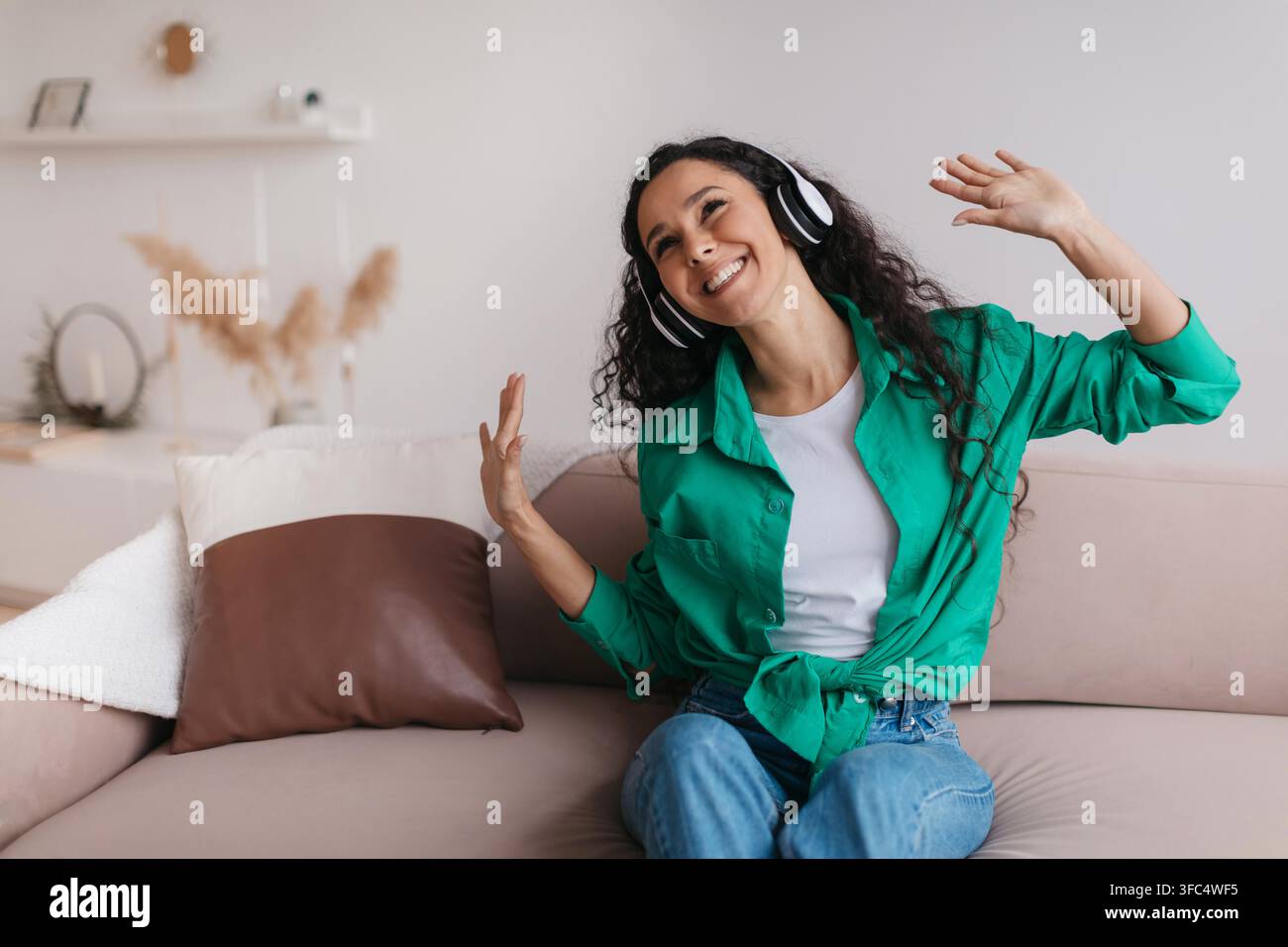 Glückliche junge Frau tanzt und hört Musik auf der Couch zu Hause, Wellness-Konzept Stockfoto