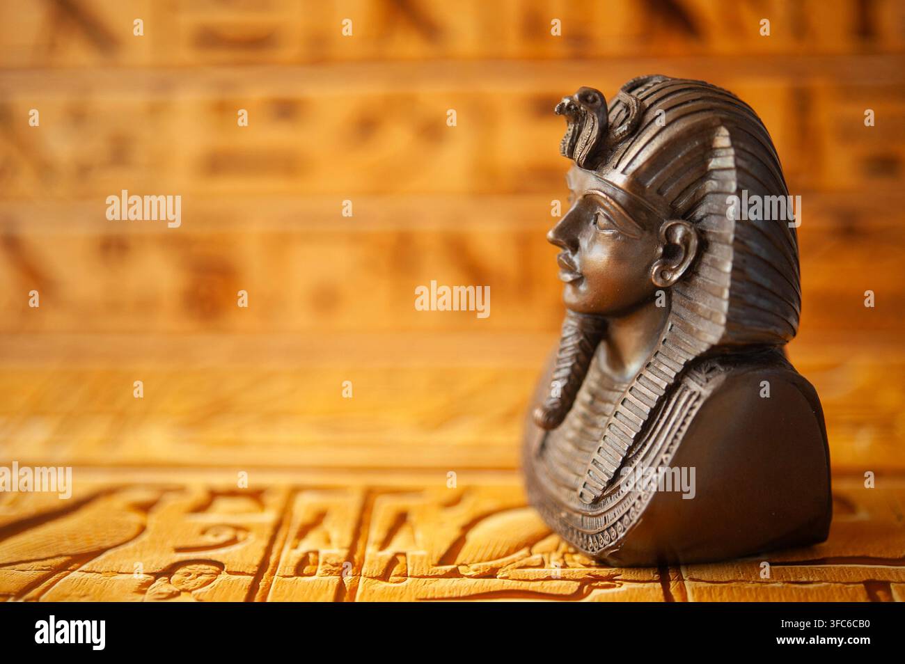 Dekorativer ägyptischer Pharaonen-Büste in Bronzetönen vor einem warmen goldenen Hieroglyphen-Hintergrund, fotografiert mit geringer Schärfentiefe Stockfoto