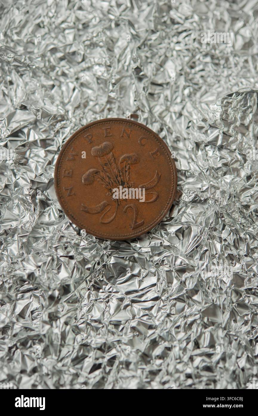Britische Zwei-Pence-Münze, die auf zerknittertem Aluminiumfolie steht, kontrastiert Kupfermünzen mit einem reflektierenden silbernen Metallhintergrund Stockfoto