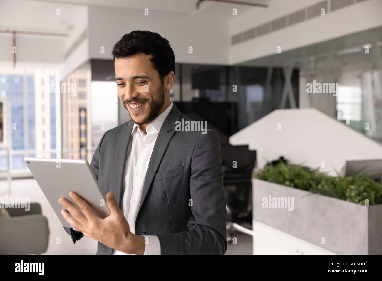 Lächelnder Nahost-Geschäftsmann, der in einem Firmenbüro an einem digitalen Tablet arbeitet Stockfoto