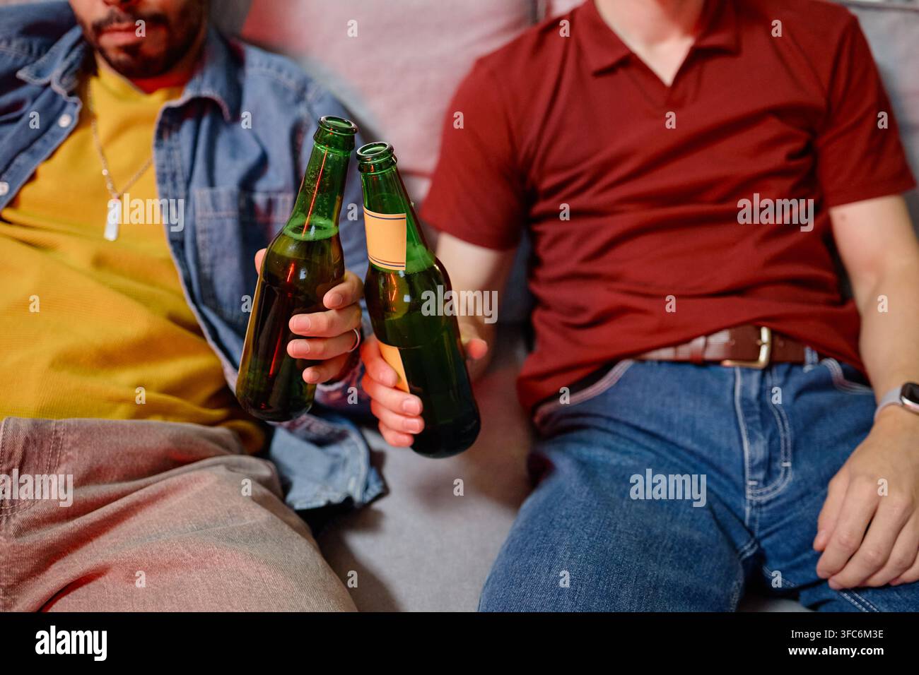 Männliche Fußballfans stoßen Bierflaschen an, während sie das Spiel beobachten Stockfoto