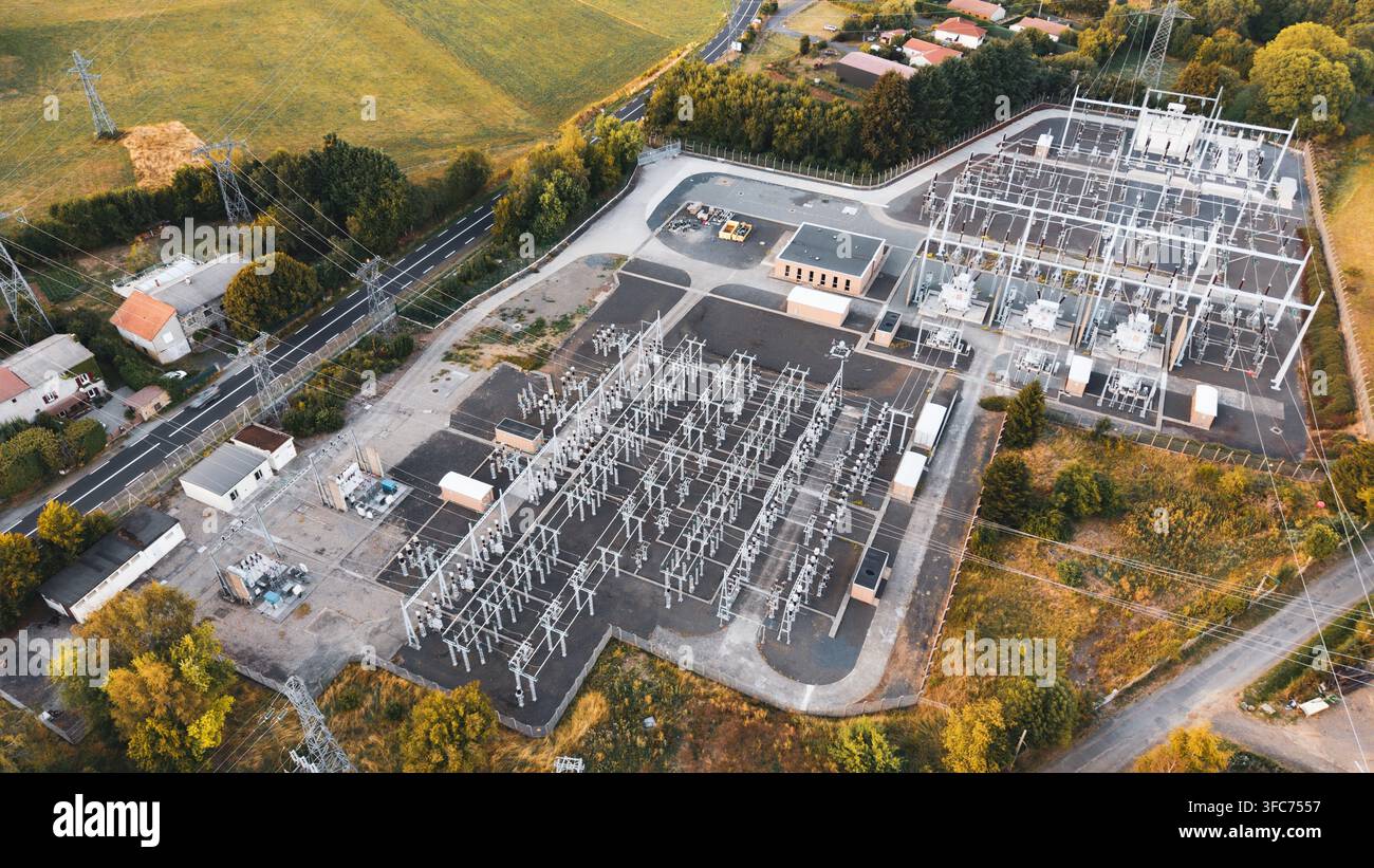 Luftaufnahme eines Umspannwerks mit Metallkonstruktionen, Transformatoren und Stromleitungen, umgeben von Bäumen und ländlichen Straßen in Orcines, Auvergne- Stockfoto