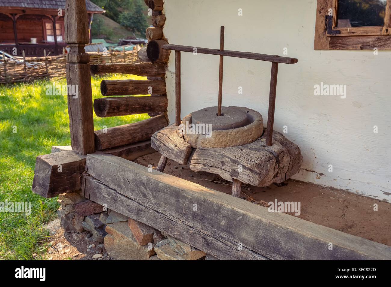 Traditionelle steinerne Handmühle auf einer rustikalen Veranda neben einem alten Landhaus in Rumänien Stockfoto