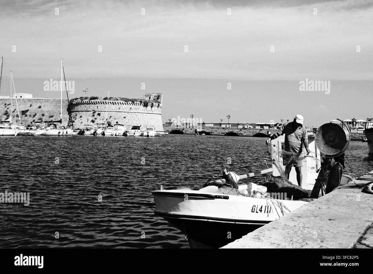Fischerboot im Hafen von Gallipoli, Puglia, Italien, mit dem Rivellino-Schloss und der Brücke zur historischen Insel im Hintergrund. Stockfoto