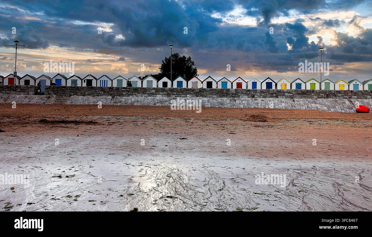Bunte Strandhütten bei Sonnenuntergang mit einem dramatischen Himmel. Stockfoto